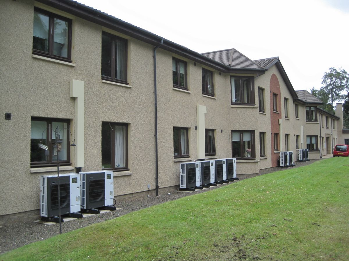 A row of air source heat pump units along the wall of a block of flats in Galashiels, Scotland